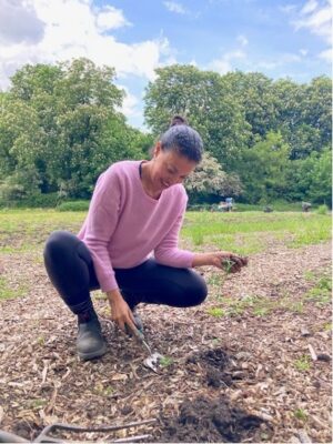 Danielle is shown outdoors in her flower plot planting seedlings into freshly prepared earth.