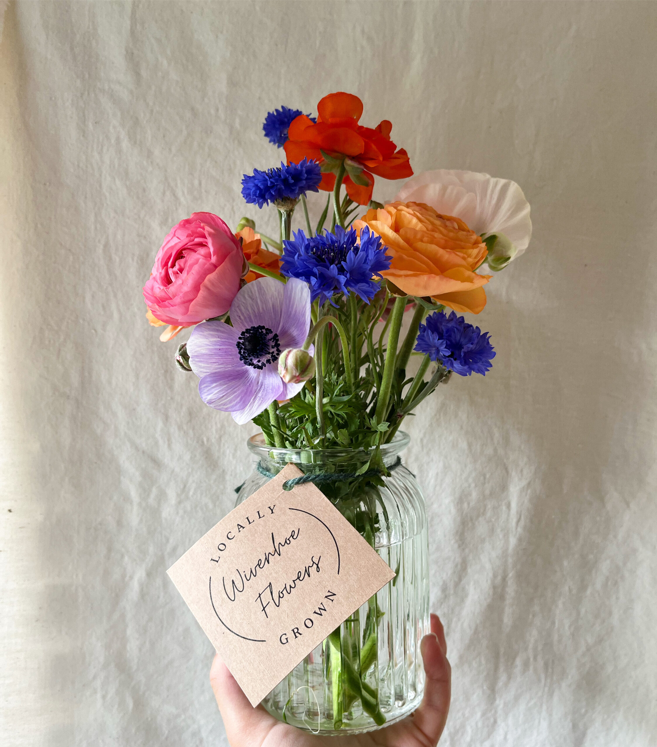 A jam jar of spring blooms from Wivenhoe Flowers, featuring anemones, ranunculus, and cornflowers.