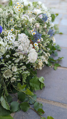 A meadow inspired white funeral casket spray for a man who loved the countryside.