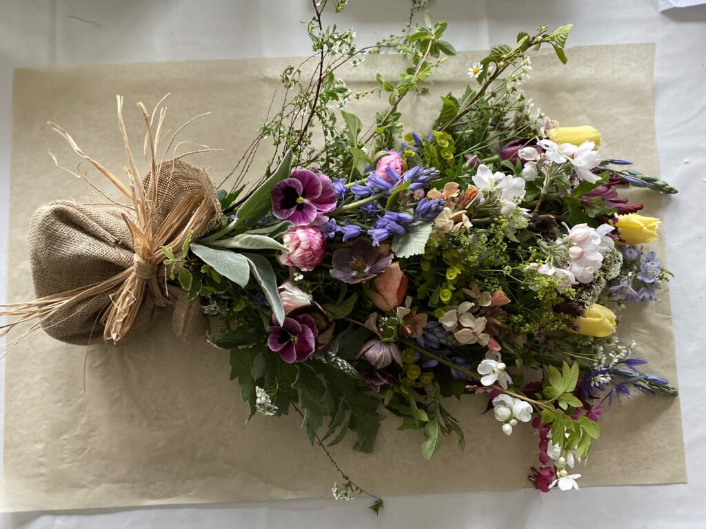 A natural funeral sheaf with seasonal spring flowers: tulips, bluebells, pansies and blossom. By Henthorn Farm Flowers.