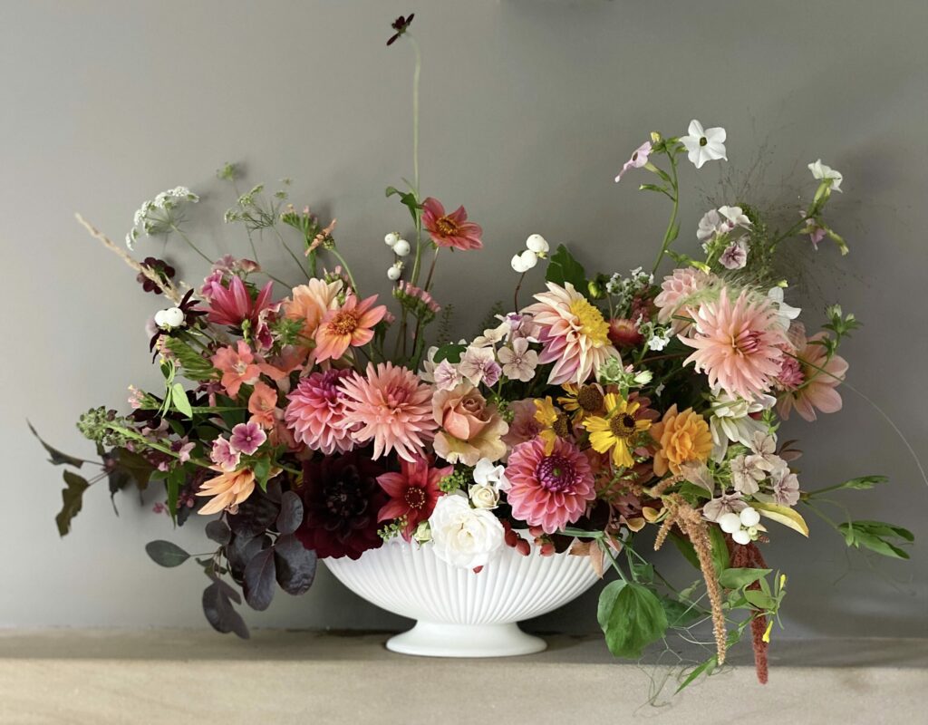 A Constance Spry inspired white ceramic windowsill vase reminiscent of the 1930s filled with an array of freshly picked dahlias from the Henthorn Farm Flowers cutting garden.