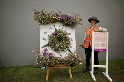 Kathryn Cronin of Fierce Blooms stands next to her floral compass installation decorated with fresh and dried flowers at RHS Chelsea 2023