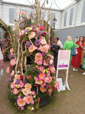 An abstract display of pink and coral peonies, purple alliums and handwoven 'roots' by Floral Media at RHS Chelsea 2023.