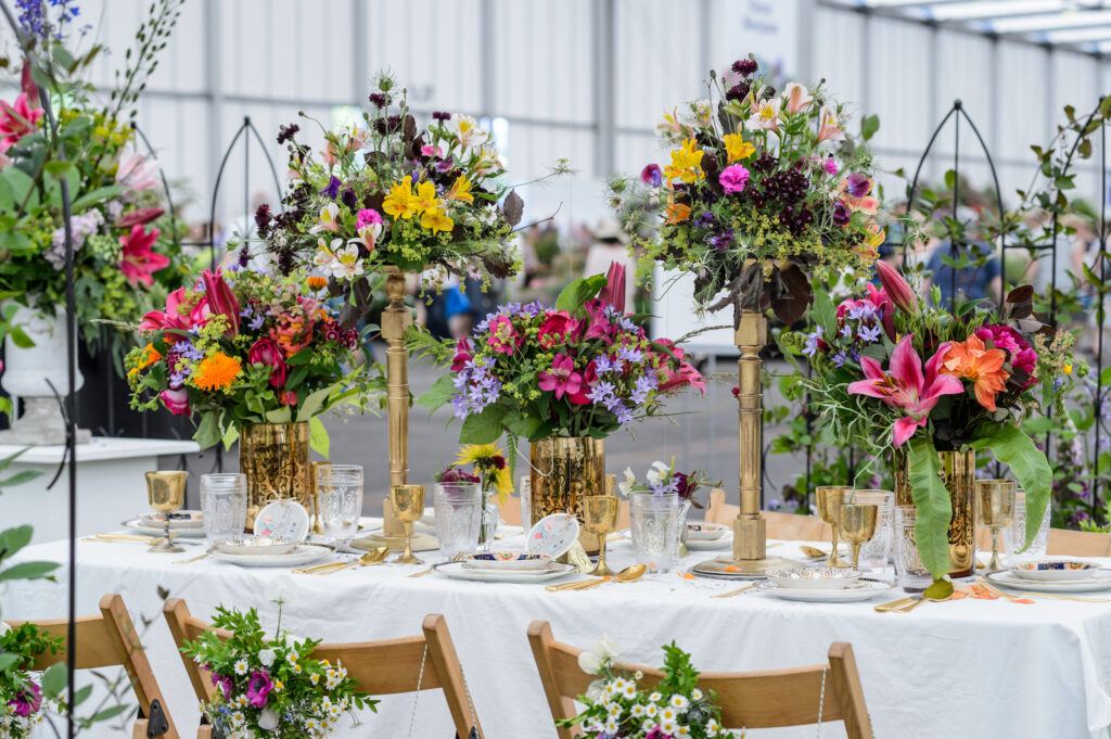 A celebration table filled with gold stands of wild, bright flowers at BBC Gardeners World Live. Flowers adorn the chair backs ready for the party. Photo: Jason Ingram.
