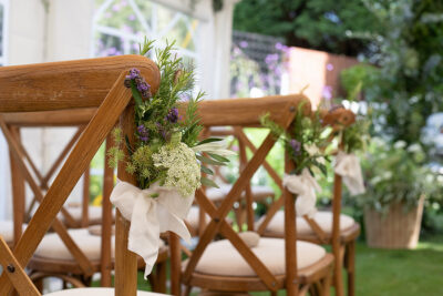 Posies of garden gathered locally grown flowers are tied to chairs with silk ribbon to line the aisle at this intimate back garden wedding.