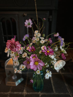 A bouquet of pink and white October flowers sits on a terracotta tiled surface against a dark background.