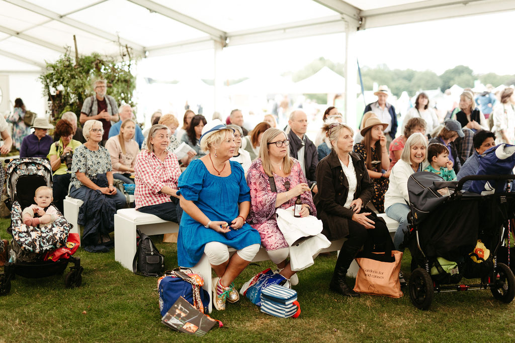 An attentive audience sit on wooden chairs to watch at Flowers from the Farm sustainable floristry demonstration in the floral marquee at RHS Tatton 2023