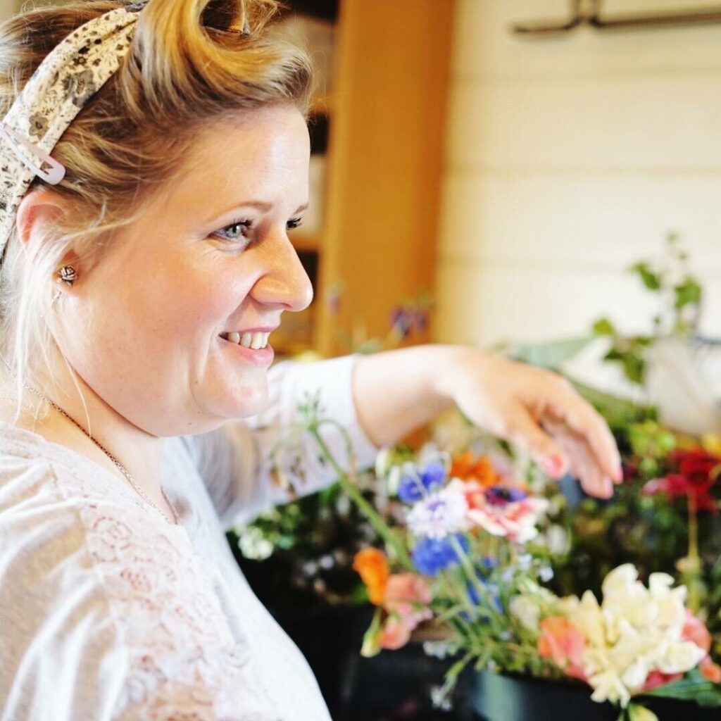 Alison of The Flower Farm smiles as she prepares bridesmaid and bridal bouquet for a wildflower style wedding.