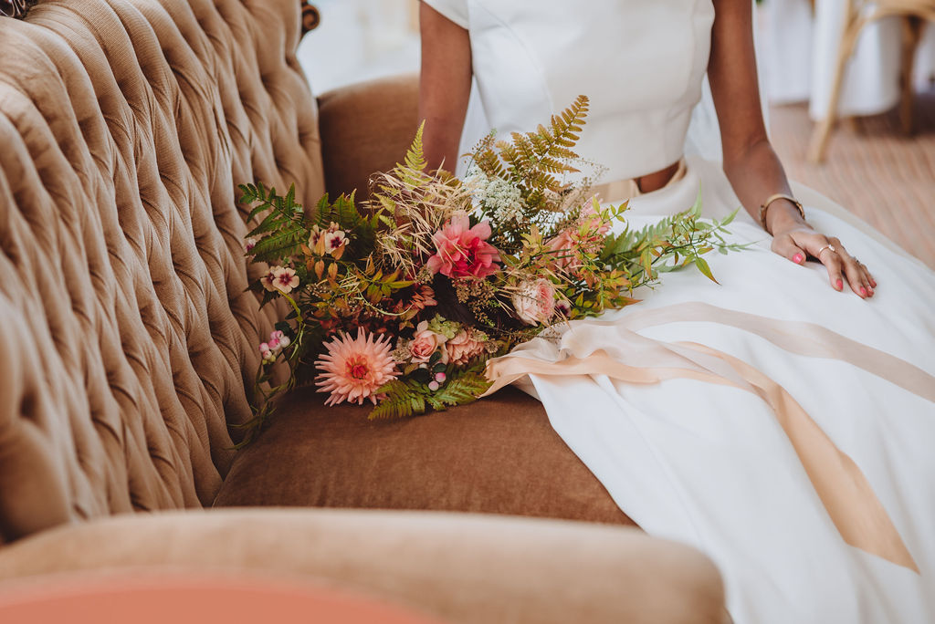 A bouquet of autumn dahlias rests on a button back sofa. Flowers by the Flower Patch. Photo by Megan Wilson Photography.