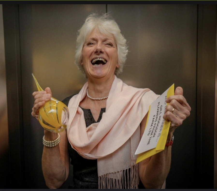 Gill holding a glass trophy and bottle of champagne as she celebrates being named Mentor of the Year in the Northern Powerhouse Awards.