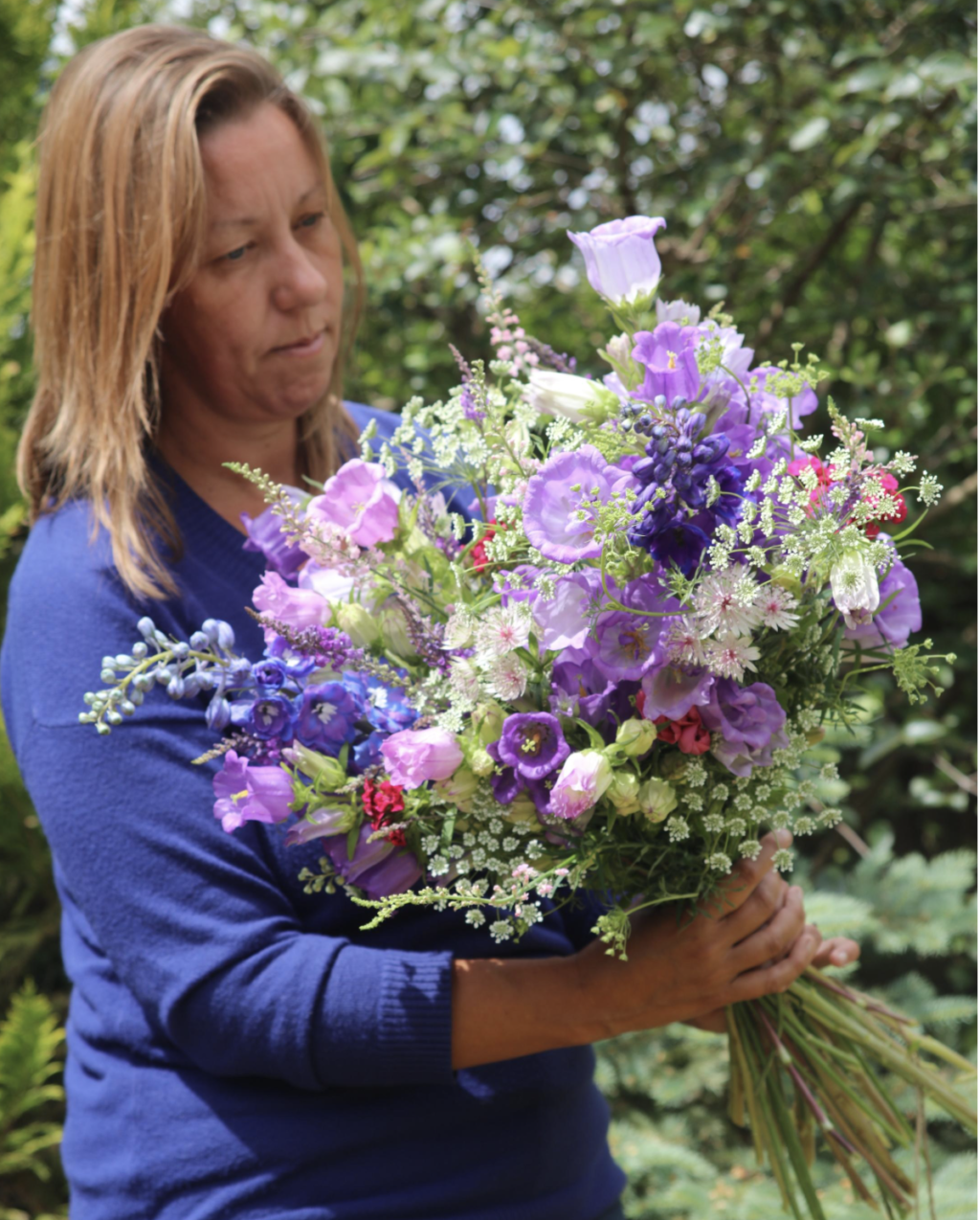 Debbie of Nature's Posy, Cambridgshire, holds an abundant meadow style bouquet filled with freshly cut British flowers from her flower farm. It's filled with the pretty purples of Canterbury Bells,starry pale pink astrantia, frothy white ammi majus and the stately blue spires of delphiniums.