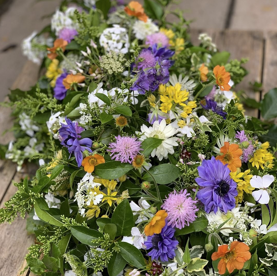 A seasonal casket arrangement of British flowers designed by The Posy Patch